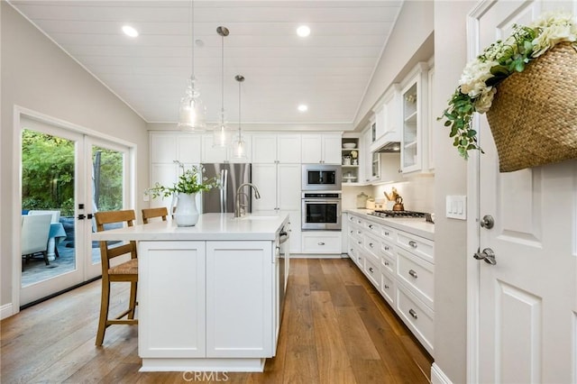 kitchen featuring white cabinetry, stainless steel appliances, a kitchen island with sink, vaulted ceiling, and light hardwood / wood-style flooring