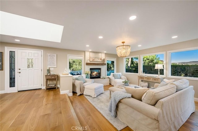 living room featuring light wood-type flooring, a brick fireplace, a skylight, and a notable chandelier