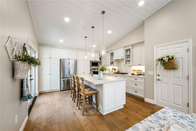 kitchen with light hardwood / wood-style flooring, white cabinetry, stainless steel appliances, hanging light fixtures, and a center island with sink