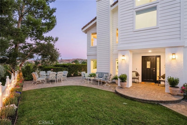 back house at dusk featuring a patio area, a yard, and an outdoor hangout area