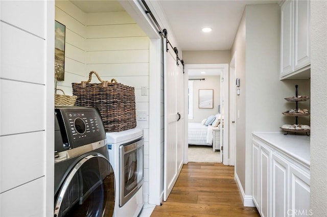 laundry area featuring a barn door, wooden walls, separate washer and dryer, cabinets, and light hardwood / wood-style flooring