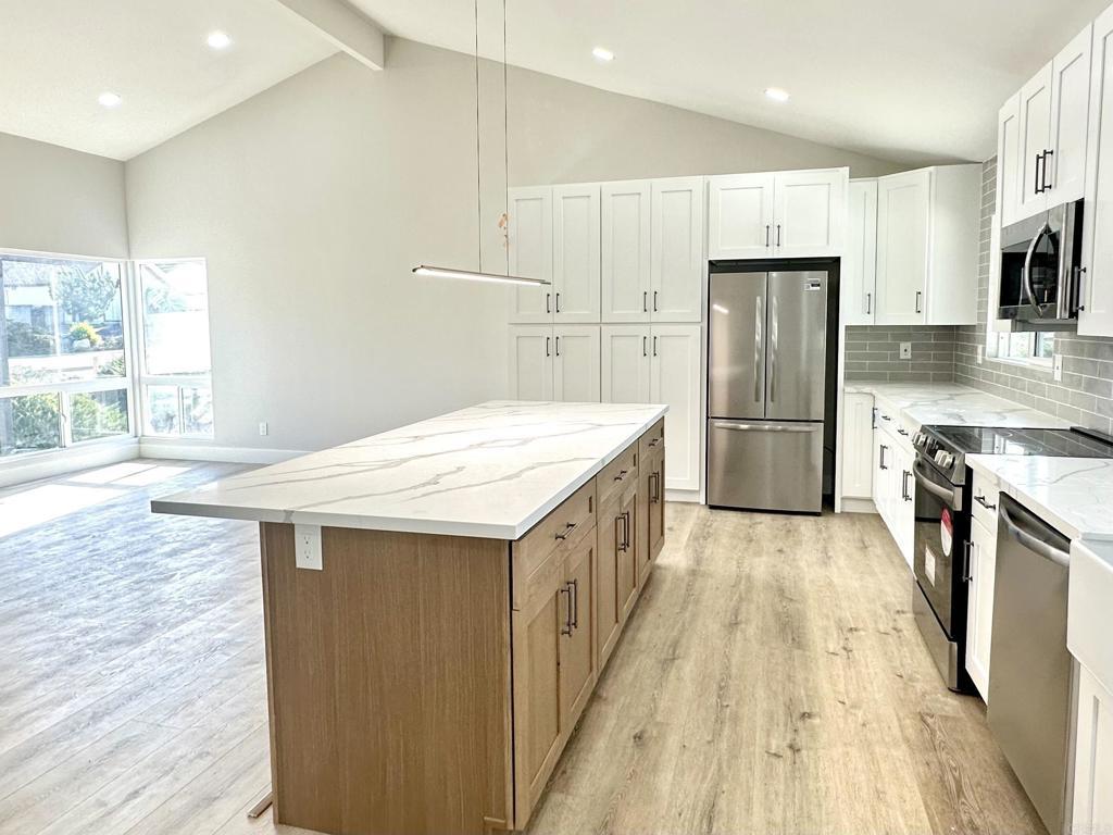 kitchen with stainless steel appliances, white cabinets, decorative backsplash, light stone countertops, and a kitchen island