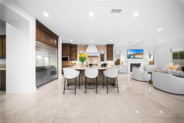 kitchen with custom exhaust hood, a large island, a kitchen breakfast bar, light stone countertops, and built in appliances