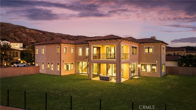 back house at dusk featuring a mountain view, a yard, and a balcony