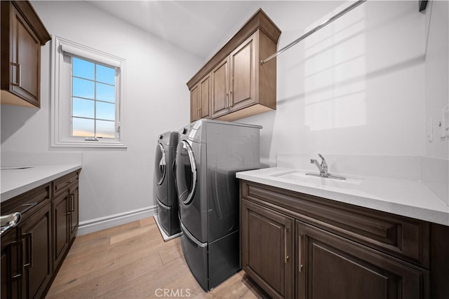 clothes washing area featuring cabinets, sink, washer and clothes dryer, and light hardwood / wood-style flooring