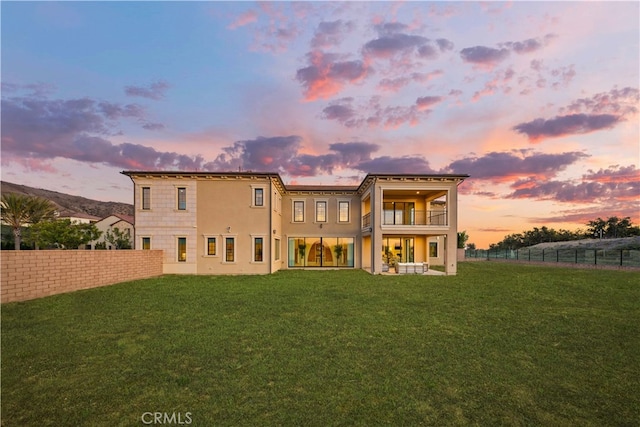 back house at dusk with a balcony and a lawn