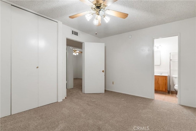 unfurnished bedroom featuring ceiling fan, ensuite bathroom, a textured ceiling, light carpet, and a closet