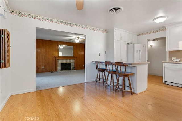 kitchen featuring white appliances, white cabinets, a fireplace, light hardwood / wood-style floors, and a breakfast bar