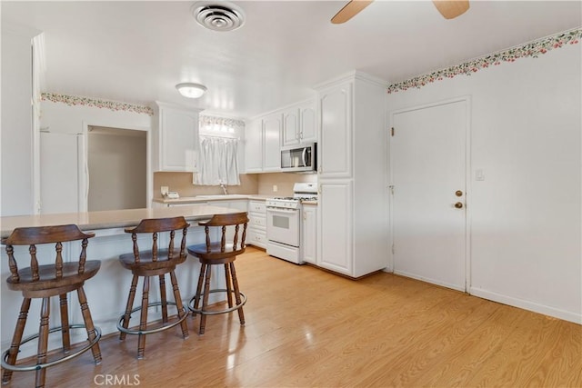 kitchen with white appliances, a kitchen bar, white cabinetry, light hardwood / wood-style floors, and ceiling fan