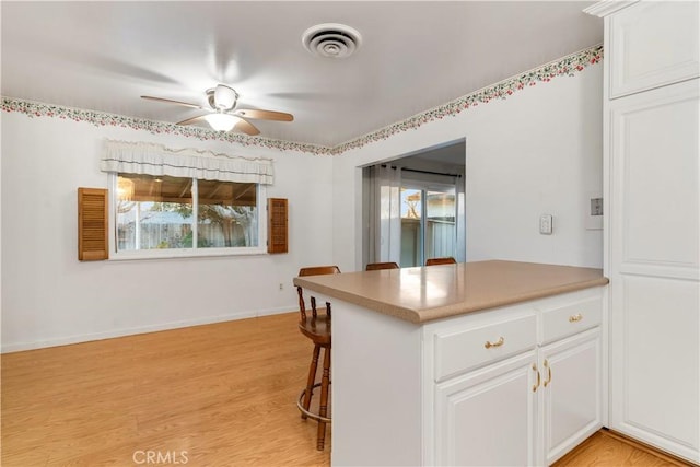 kitchen with white cabinets, kitchen peninsula, ceiling fan, a breakfast bar, and light hardwood / wood-style flooring