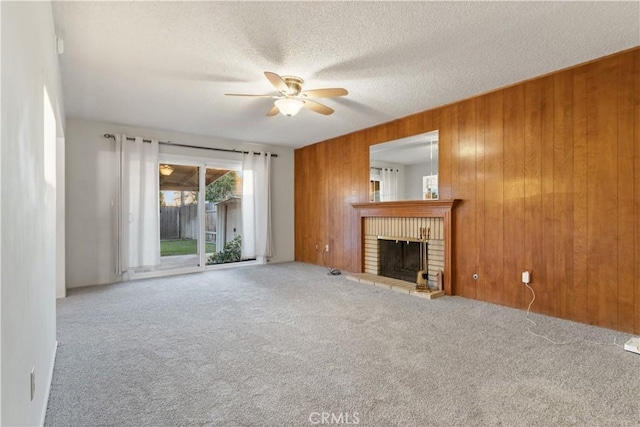 unfurnished living room featuring a textured ceiling, ceiling fan, wood walls, carpet flooring, and a brick fireplace