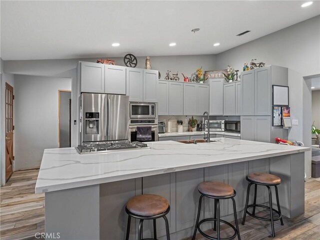 20276 Waco Rd, Apple Valley, CA 92308 - kitchen featuring lofted ceiling, a kitchen island with sink, light stone countertops, a breakfast bar area, and stainless steel appliances