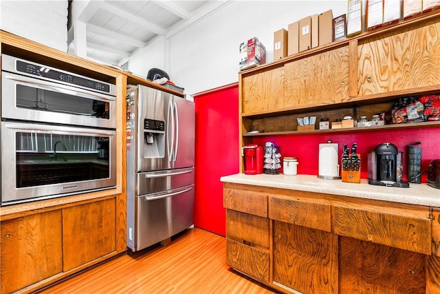 kitchen featuring stainless steel appliances, light hardwood / wood-style flooring, and beamed ceiling