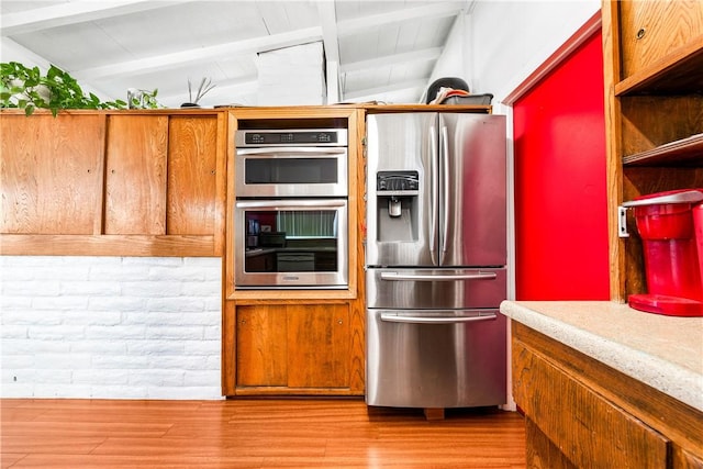 kitchen featuring appliances with stainless steel finishes, light hardwood / wood-style flooring, and vaulted ceiling with beams