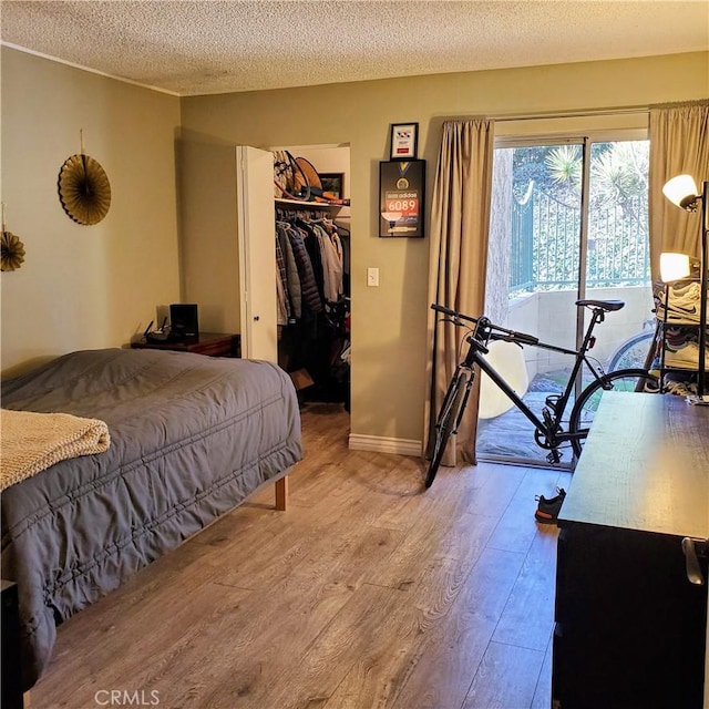 bedroom featuring a spacious closet, a textured ceiling, hardwood / wood-style flooring, a closet, and access to outside