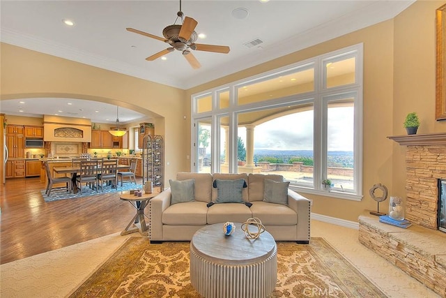 living room with crown molding, ceiling fan, a fireplace, and light hardwood / wood-style flooring