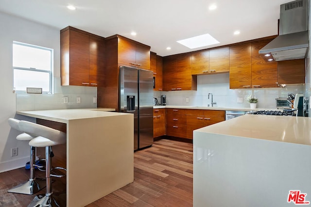 kitchen with sink, a breakfast bar area, a skylight, stainless steel appliances, and wall chimney exhaust hood