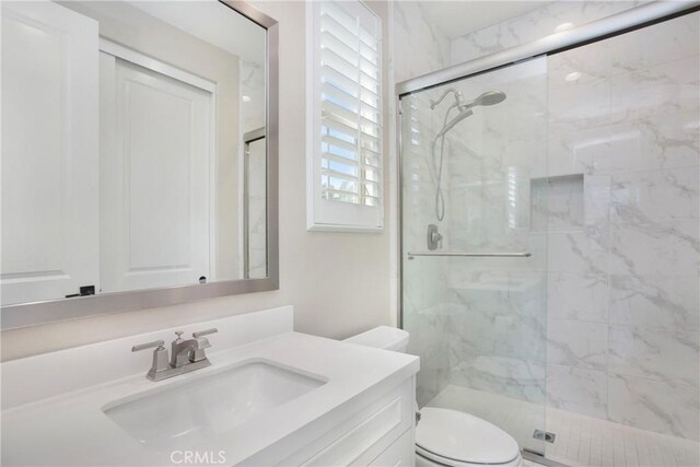 bathroom featuring a shower with shower door, vanity, and toilet