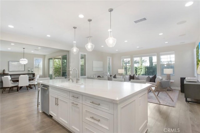 kitchen featuring an island with sink, decorative light fixtures, white cabinets, light hardwood / wood-style flooring, and sink