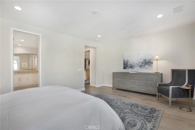 bedroom featuring a spacious closet, a closet, connected bathroom, and light hardwood / wood-style flooring