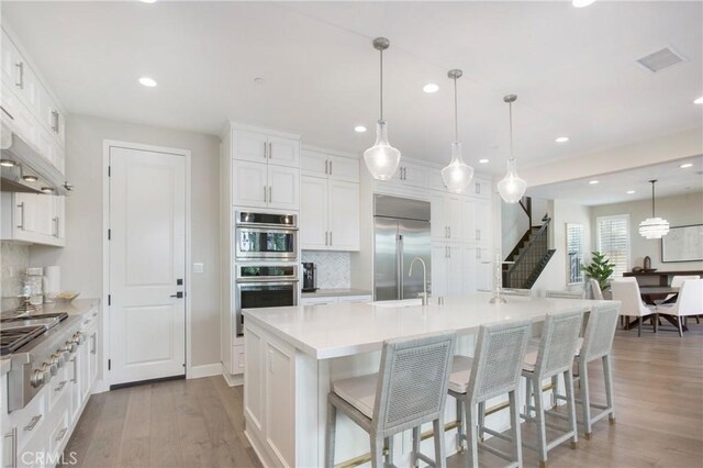 kitchen with stainless steel appliances, decorative backsplash, hanging light fixtures, a large island with sink, and white cabinets