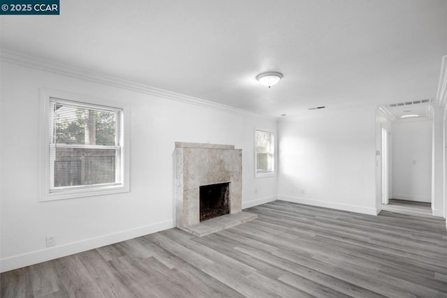 unfurnished living room featuring a tiled fireplace, light hardwood / wood-style floors, crown molding, and a healthy amount of sunlight