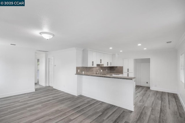 kitchen featuring sink, white cabinets, ornamental molding, light hardwood / wood-style floors, and kitchen peninsula