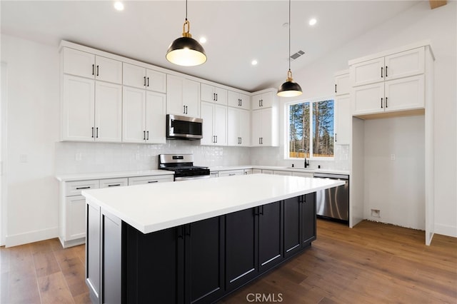 kitchen featuring hanging light fixtures, stainless steel appliances, white cabinets, and a kitchen island