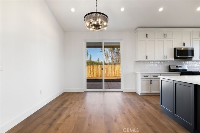 kitchen featuring decorative backsplash, hanging light fixtures, stainless steel appliances, white cabinets, and a chandelier