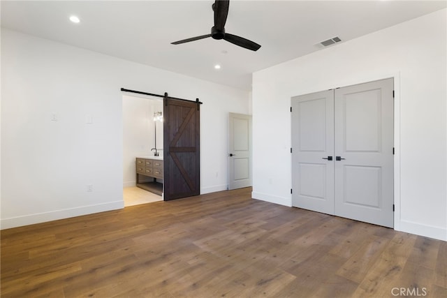 unfurnished bedroom with ceiling fan, a barn door, connected bathroom, and light hardwood / wood-style floors