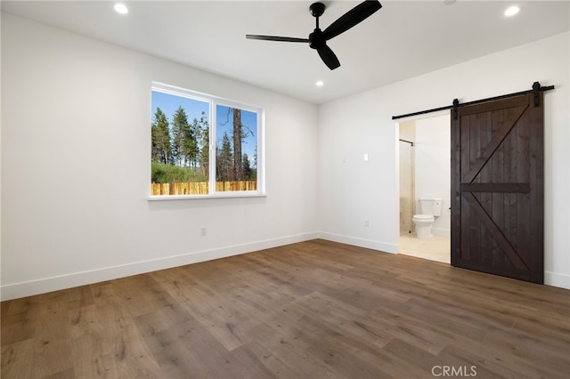 unfurnished bedroom featuring connected bathroom, ceiling fan, a barn door, and hardwood / wood-style floors