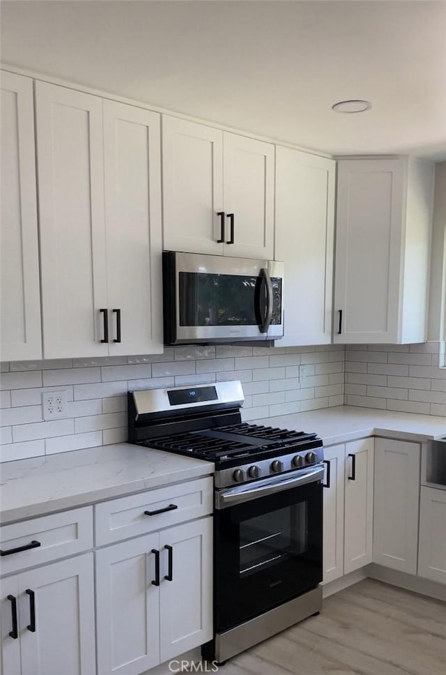 kitchen with white cabinets, stainless steel appliances, light hardwood / wood-style floors, and tasteful backsplash