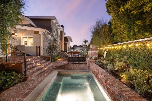 pool at dusk featuring pool water feature and a patio