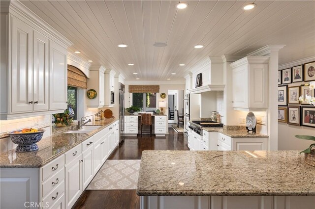 kitchen with wooden ceiling, white cabinets, light stone counters, and sink