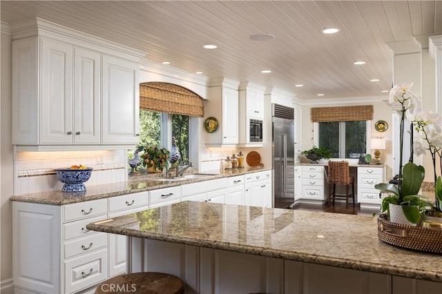 kitchen featuring light stone counters, wooden ceiling, white cabinets, and built in appliances