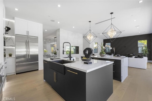 kitchen featuring white cabinets, built in refrigerator, a kitchen island with sink, and pendant lighting