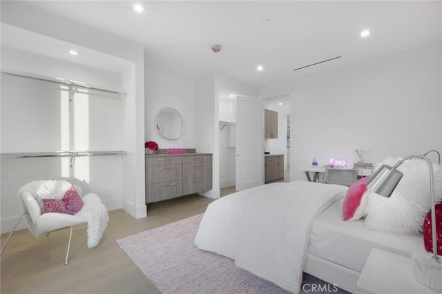 bedroom with a spacious closet, light wood-type flooring, and connected bathroom