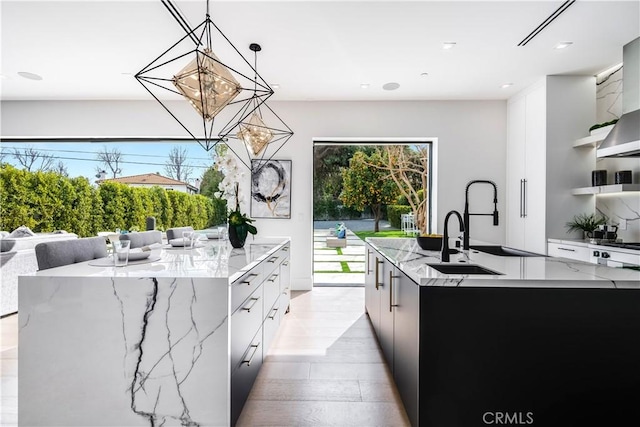 kitchen with light stone counters, a spacious island, white cabinetry, and hanging light fixtures