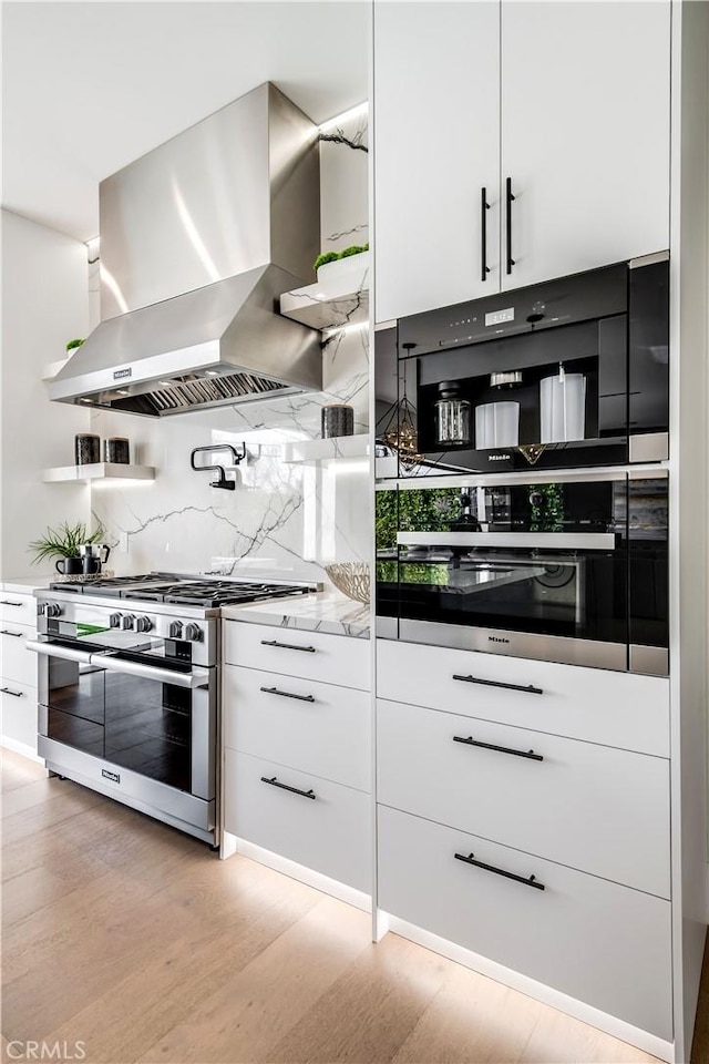 kitchen with stainless steel appliances, white cabinetry, light hardwood / wood-style floors, light stone countertops, and island range hood