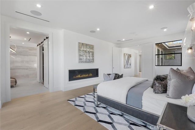 bedroom featuring ensuite bath, a barn door, and light hardwood / wood-style flooring