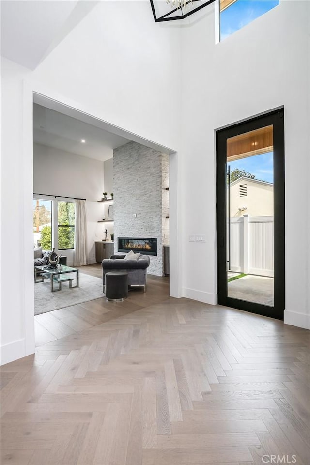 unfurnished living room featuring a high ceiling, a fireplace, and light parquet floors