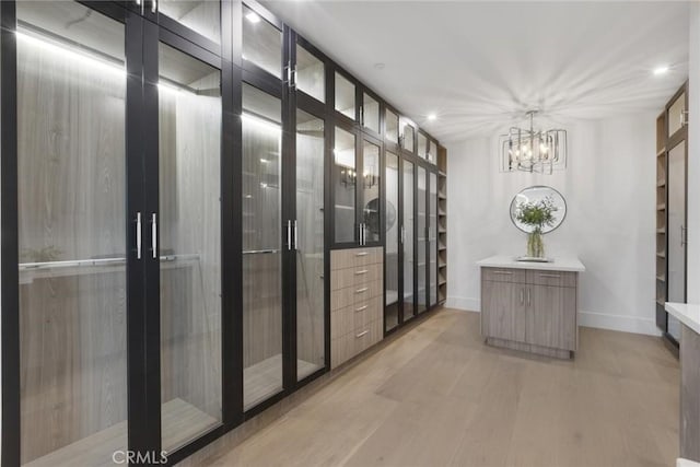 walk in closet with french doors, a chandelier, and light hardwood / wood-style flooring