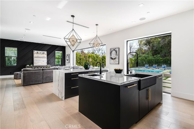 kitchen with sink, light hardwood / wood-style floors, decorative light fixtures, and a center island with sink