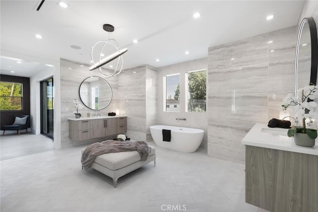 bathroom with vanity, tile walls, a chandelier, and a bath