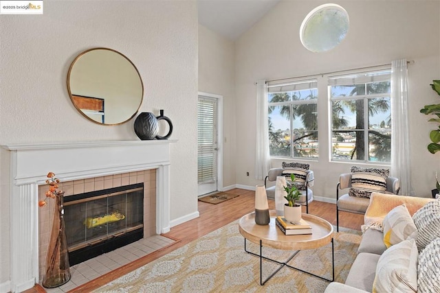 living room featuring light hardwood / wood-style flooring, a tile fireplace, and high vaulted ceiling