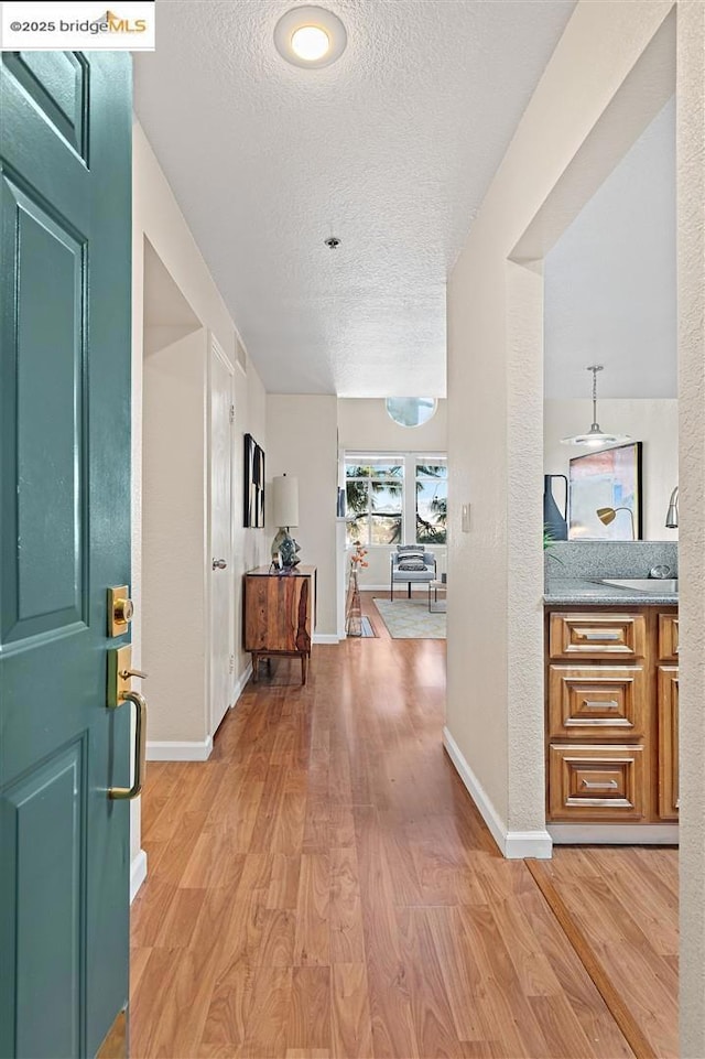 corridor with a textured ceiling and light hardwood / wood-style flooring