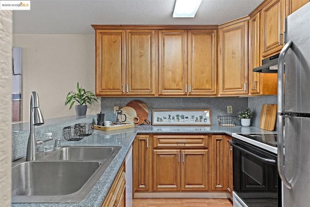 kitchen featuring range with electric cooktop, light wood-type flooring, stainless steel refrigerator, dark stone counters, and sink