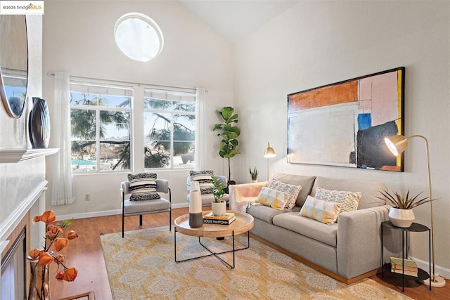 living area with high vaulted ceiling, a tiled fireplace, and light wood-type flooring