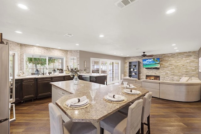 kitchen with a breakfast bar, a large fireplace, dark brown cabinetry, and a center island