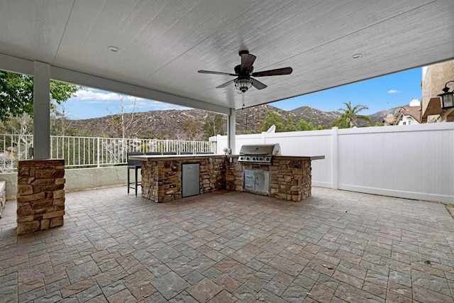 view of patio featuring ceiling fan, a bar, a mountain view, and grilling area